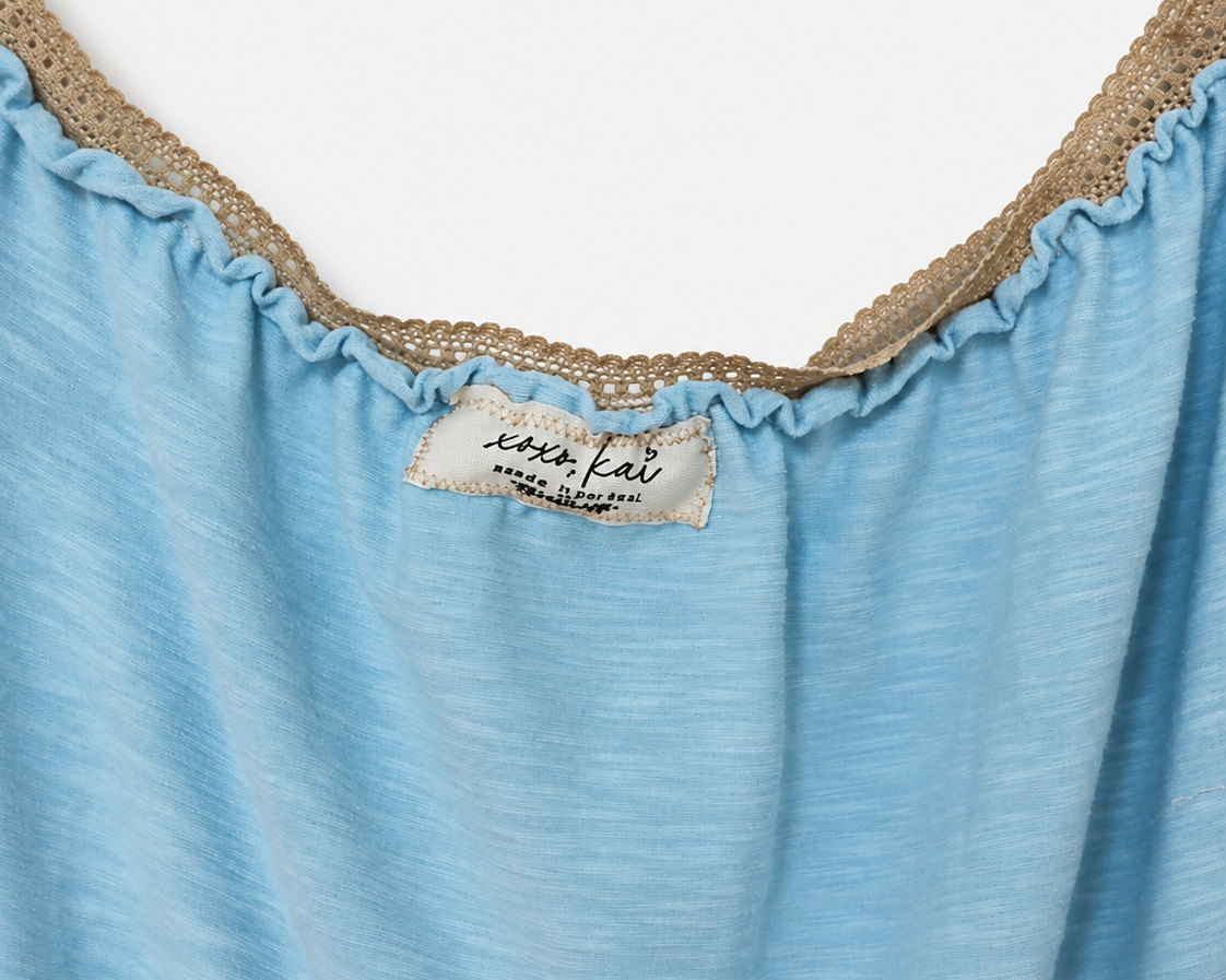 Close-up of a light blue top with a ruffled neckline trimmed in beige lace, featuring a visible 'sophia fair' brand label.