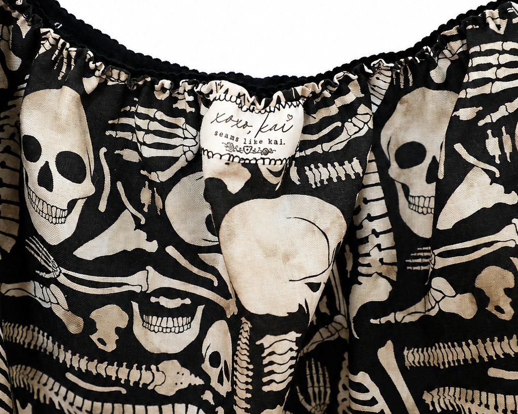 Close-up of a black garment with an all-over cream skeleton print, featuring a ruffled neckline and a visible fabric label that reads 'Letter Left London'.