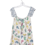 A baby romper hanging on a clear plastic hanger against a white wall. The romper features a cream-colored body with a colorful dinosaur print in shades of blue, green, yellow, and pink, and has light blue and white gingham checkered shoulder straps.