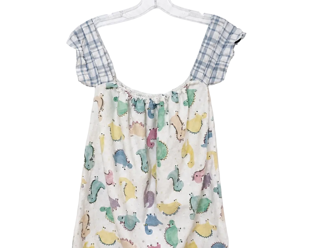 A baby romper hanging on a clear plastic hanger against a white wall. The romper features a cream-colored body with a colorful dinosaur print in shades of blue, green, yellow, and pink, and has light blue and white gingham checkered shoulder straps.