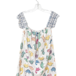 A children's sleeveless romper hanging on a clear plastic hanger against a plain white background. The romper has a white base with a colorful print of cartoon dinosaurs and has blue-and-white plaid shoulder straps.