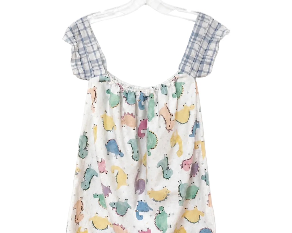 A children's sleeveless romper hanging on a clear plastic hanger against a plain white background. The romper has a white base with a colorful print of cartoon dinosaurs and has blue-and-white plaid shoulder straps.