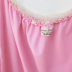 Close-up of a pink garment with a ruffled neckline trimmed in cream lace, showing a small sewn label.