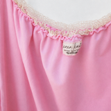 Close-up of a pink garment with a ruffled neckline trimmed in cream lace, showing a small sewn label.