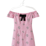 A pink off-the-shoulder dress with a black bow at the neckline and small floral embroidery, hanging on a clear plastic hanger against a white background.