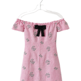 A pink off-the-shoulder dress with a black bow at the neckline and small floral embroidery, hanging on a clear plastic hanger against a white background.