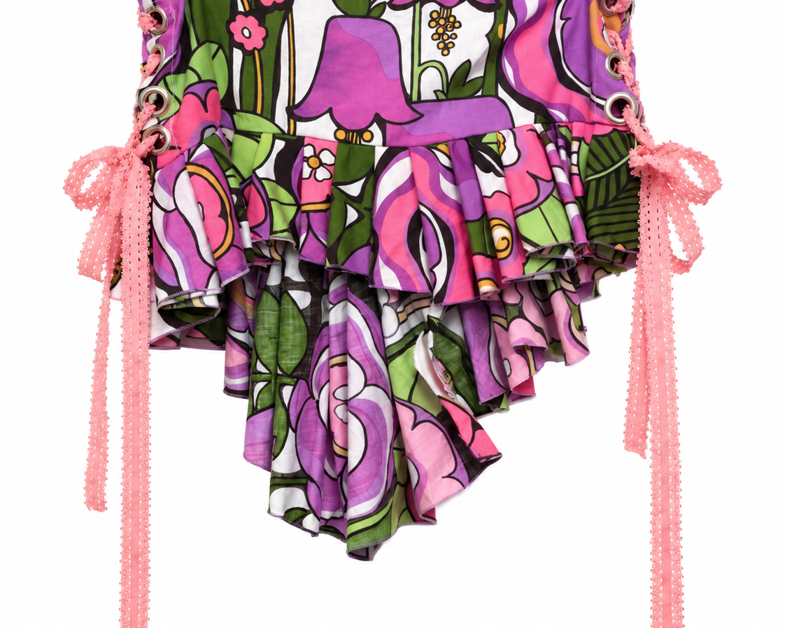 A ruffled bikini bottom featuring a vibrant pink, purple, and green floral and botanical print, with pink beaded side ties hanging down on a white background.