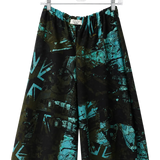 A pair of wide-leg shorts with an abstract teal and black graffiti-style print, hanging from a clear plastic hanger against a plain white wall.