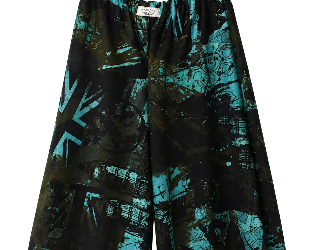 A pair of wide-leg shorts with an abstract teal and black graffiti-style print, hanging from a clear plastic hanger against a plain white wall.