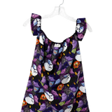 A sleeveless babydoll dress with a dark purple and black background, featuring a playful print of cartoon cats in white, purple, orange, and yellow. The dress has ruffled shoulder straps and is displayed on a clear plastic hanger against a plain white background.