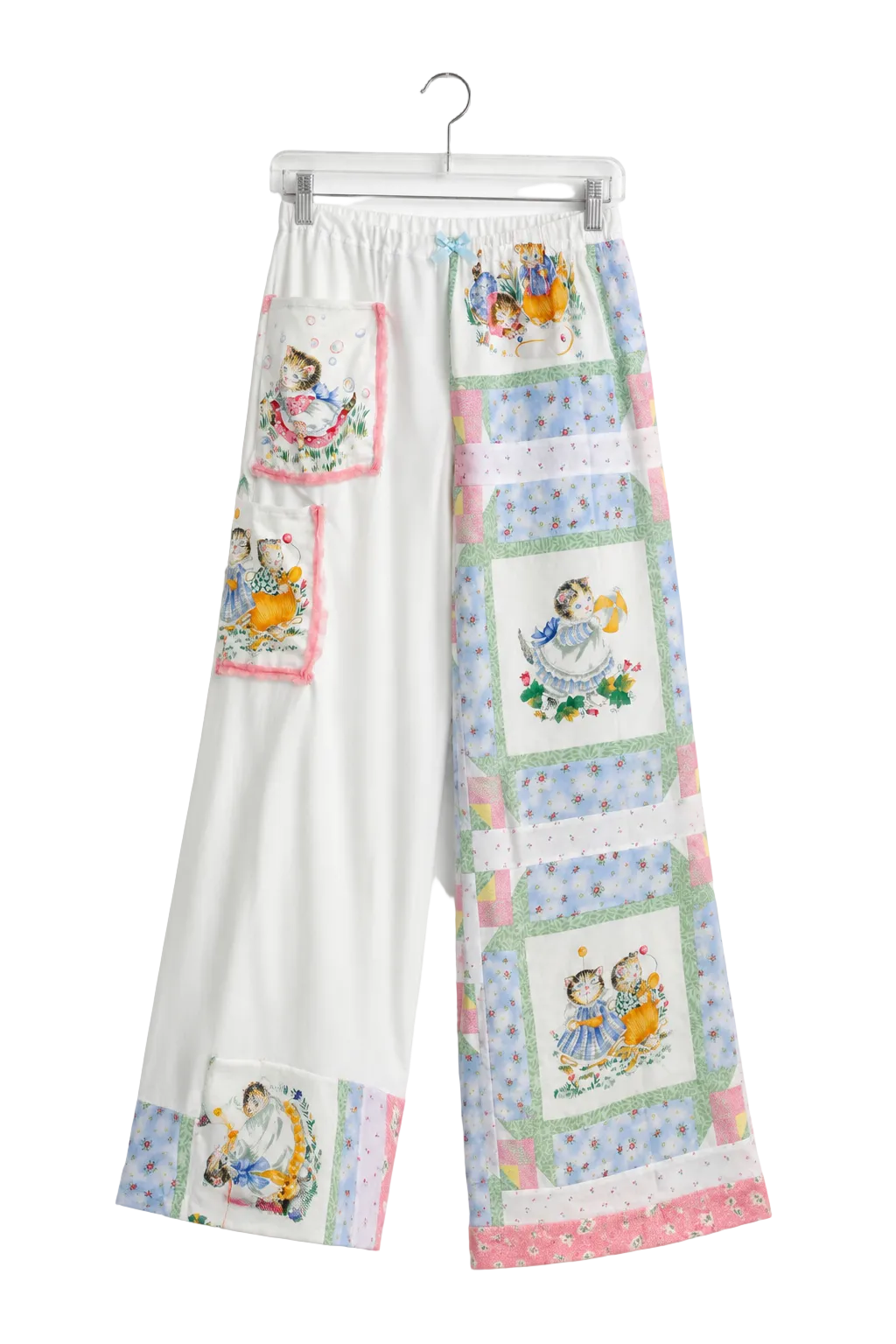White wide-leg pants with a patchwork quilt design featuring vintage illustrations of children, hanging on a clear plastic hanger against a white background.