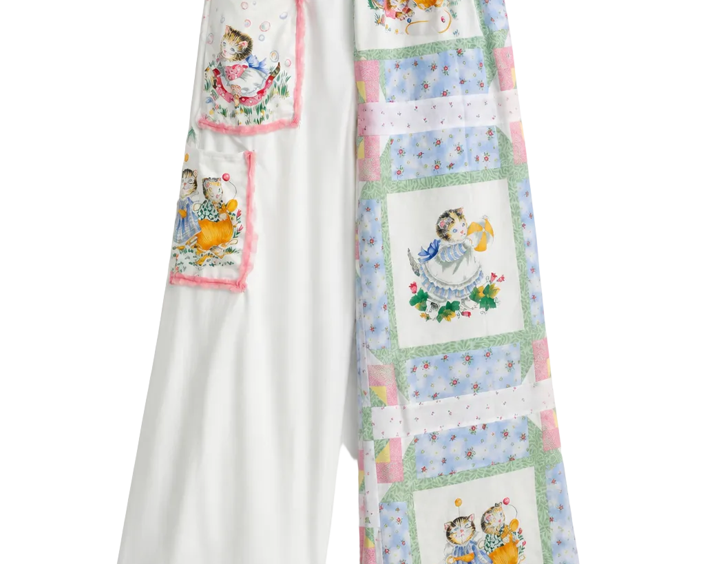 White wide-leg pants with a patchwork quilt design featuring vintage illustrations of children, hanging on a clear plastic hanger against a white background.