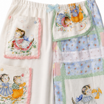 A pair of children's patchwork pajama pants featuring whimsical cartoon animal and girl illustrations, split down the middle with one side in cream fabric with pink-trimmed pockets and the other side in a pastel patchwork design.