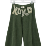 A pair of dark green wide-leg cropped pants hanging on a clear plastic hanger against a white background. The pants feature a textured, snakeskin-patterned 'xo xo' graphic across the upper front.