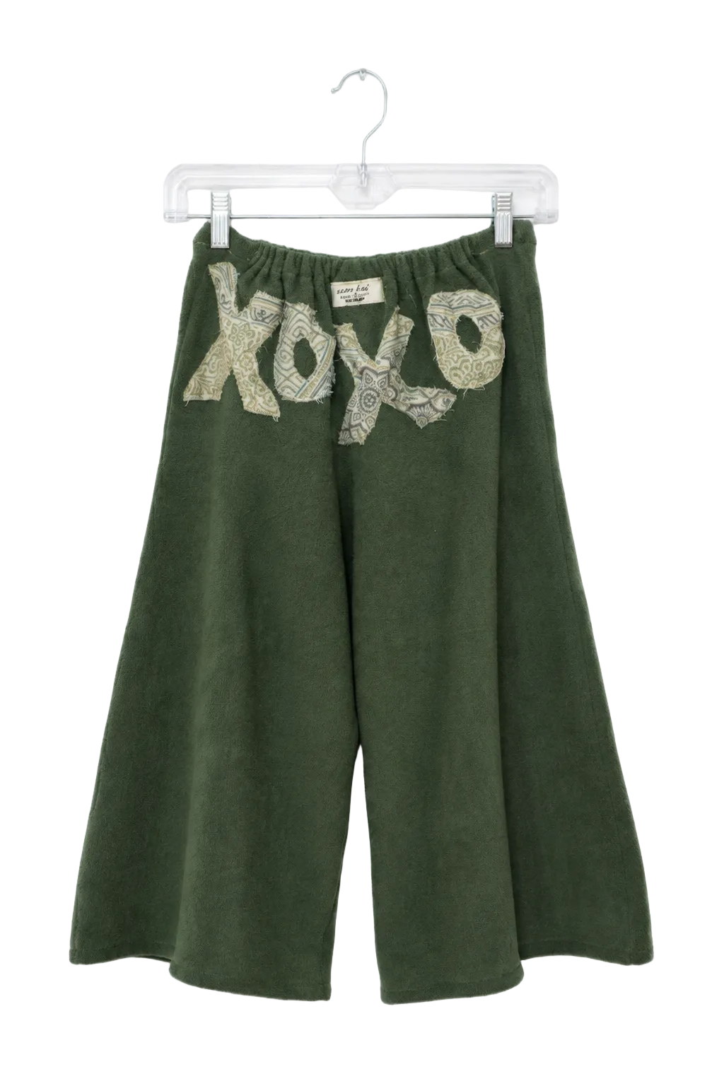 A pair of dark green wide-leg cropped pants hanging on a clear plastic hanger against a white background. The pants feature a textured, snakeskin-patterned 'xo xo' graphic across the upper front.