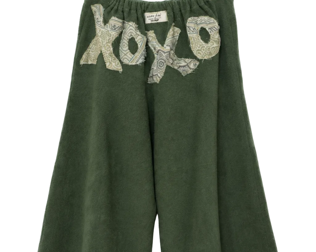 A pair of dark green wide-leg cropped pants hanging on a clear plastic hanger against a white background. The pants feature a textured, snakeskin-patterned 'xo xo' graphic across the upper front.