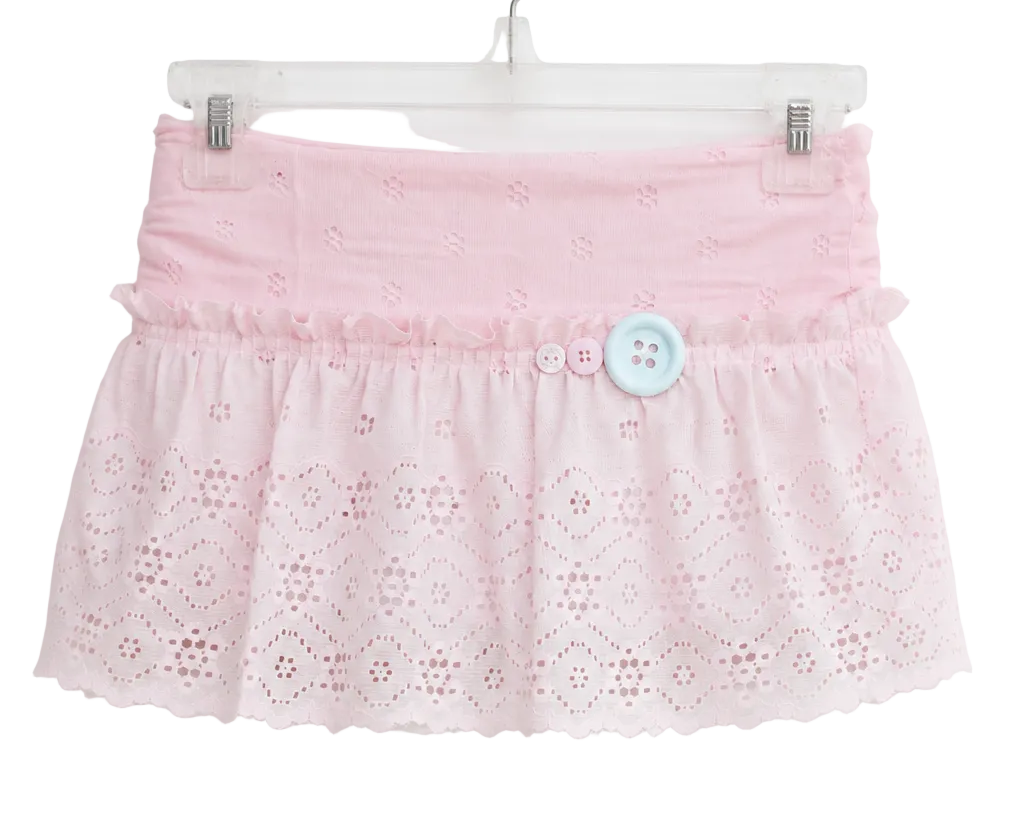 A light pink eyelet lace skirt with a ruffled waistband and a single light blue decorative button, hanging on a clear plastic hanger against a plain white background.