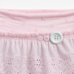 Close-up of a light pink eyelet skirt with a ruffled waistband, featuring three decorative buttons in pink and white.