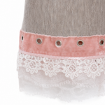 Close-up of a skirt or dress hem featuring a dusty pink velvet band with silver eyelets, layered over a white floral lace trim, on a light gray textured fabric.