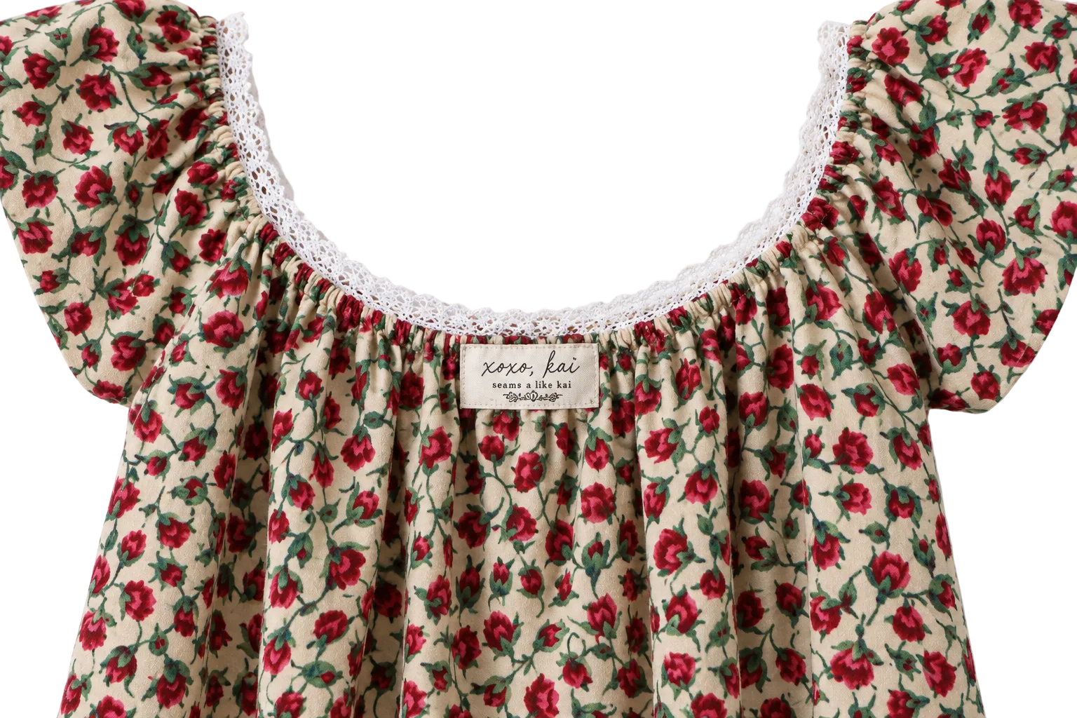 Close-up of a cream-colored blouse with a red and green floral print, featuring a white lace-trimmed scoop neckline and a visible 'xoxo kai' brand label.