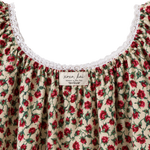 Close-up of a cream-colored blouse with a red and green floral print, featuring a white lace-trimmed scoop neckline and a visible 'xoxo kai' brand label.