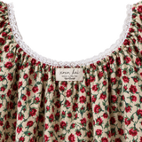 Close-up of a cream-colored blouse with a red and green floral print, featuring a white lace-trimmed scoop neckline and a visible 'xoxo kai' brand label.