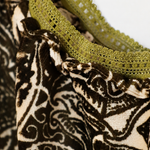 Close-up of a garment featuring a dark brown and cream paisley patterned fabric with olive green lace trim.