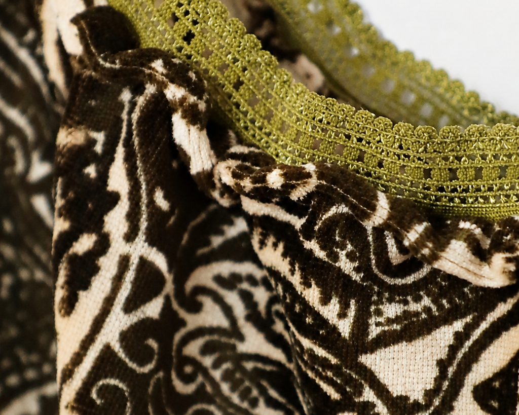 Close-up of a garment featuring a dark brown and cream paisley patterned fabric with olive green lace trim.