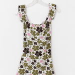 A sleeveless white babydoll dress with a green and brown clover pattern, pink floral accents, and a pink lace hem, hanging on a white plastic hanger against a white background.