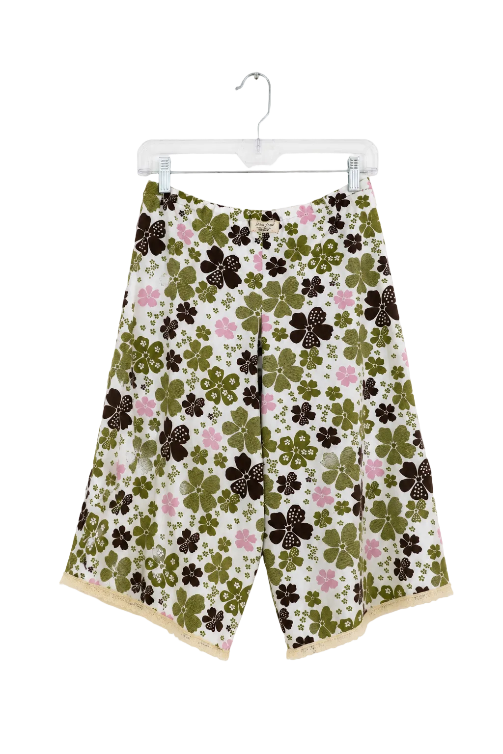 A pair of women's wide-leg shorts with a retro floral pattern featuring olive green, dark brown, and pink flowers on a cream background, hanging on a clear plastic hanger against a white wall.