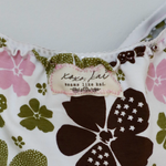 Close-up of a floral-patterned garment, likely a bikini top, featuring a white base with large dark brown and olive green flowers, pink floral accents, and a visible 'Koko Kai' brand label.