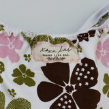 Close-up of a floral-patterned garment, likely a bikini top, featuring a white base with large dark brown and olive green flowers, pink floral accents, and a visible 'Koko Kai' brand label.
