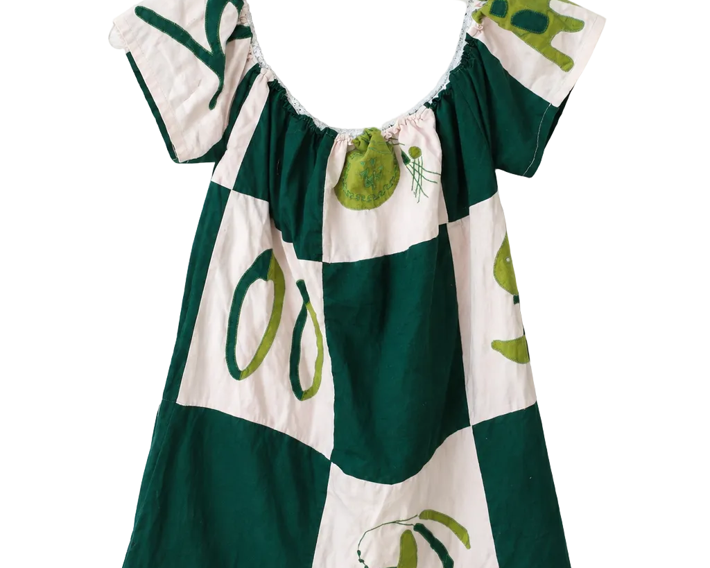 A short-sleeve dress with a green and white checkered pattern and olive illustrations, hanging on a white plastic hanger against a plain white wall.
