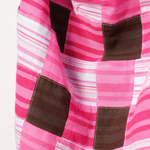 A close-up of a patchwork quilt featuring pink and white striped fabric panels with dark brown square patches.