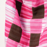 A close-up of a patchwork quilt featuring pink and white striped fabric panels with dark brown square patches.