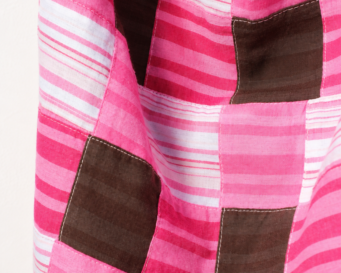A close-up of a patchwork quilt featuring pink and white striped fabric panels with dark brown square patches.