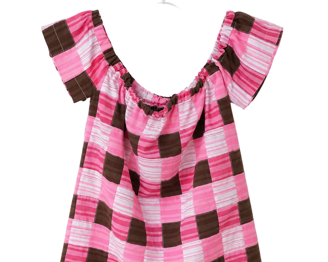 A pink and brown checkered short-sleeve top with a smocked neckline, hanging on a clear plastic hanger against a plain white background.