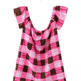 A pink and brown checkered top with ruffled cap sleeves, hanging on a white plastic hanger against a plain white wall.