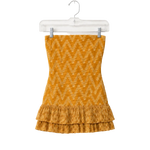 A yellow-orange knit strapless top with a zigzag pattern and a ruffled hem, hanging on a clear plastic hanger against a white background.