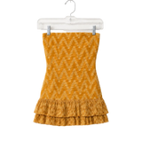 A yellow-orange knit strapless top with a zigzag pattern and a ruffled hem, hanging on a clear plastic hanger against a white background.