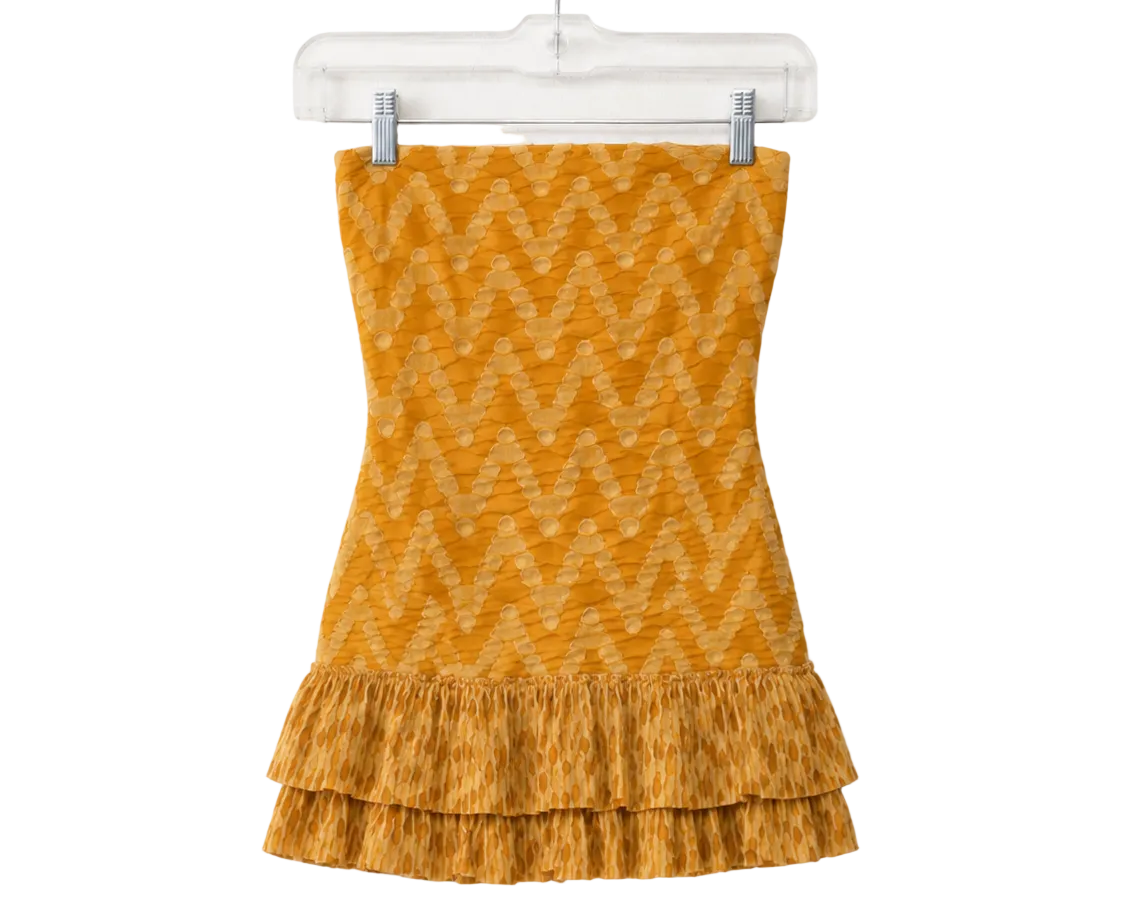 A yellow-orange knit strapless top with a zigzag pattern and a ruffled hem, hanging on a clear plastic hanger against a white background.