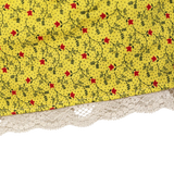 Close-up of a yellow fabric item with a small red and black floral vine print and a cream lace trim along the bottom edge, shown against a white background.