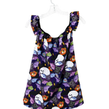 A sleeveless baby/toddler dress with ruffled shoulder straps, featuring a purple and black Halloween print of bats, ghosts, and jack-o'-lanterns, hanging on a white plastic hanger against a white background.