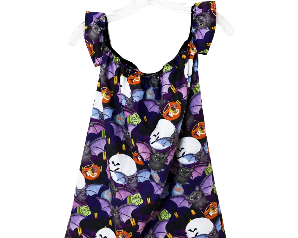 A sleeveless baby/toddler dress with ruffled shoulder straps, featuring a purple and black Halloween print of bats, ghosts, and jack-o'-lanterns, hanging on a white plastic hanger against a white background.