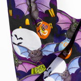 A close-up of a Halloween-themed fabric featuring a repeating pattern of cartoon bats, purple wings, orange trick-or-treat bags, and white moon shapes on a dark background.