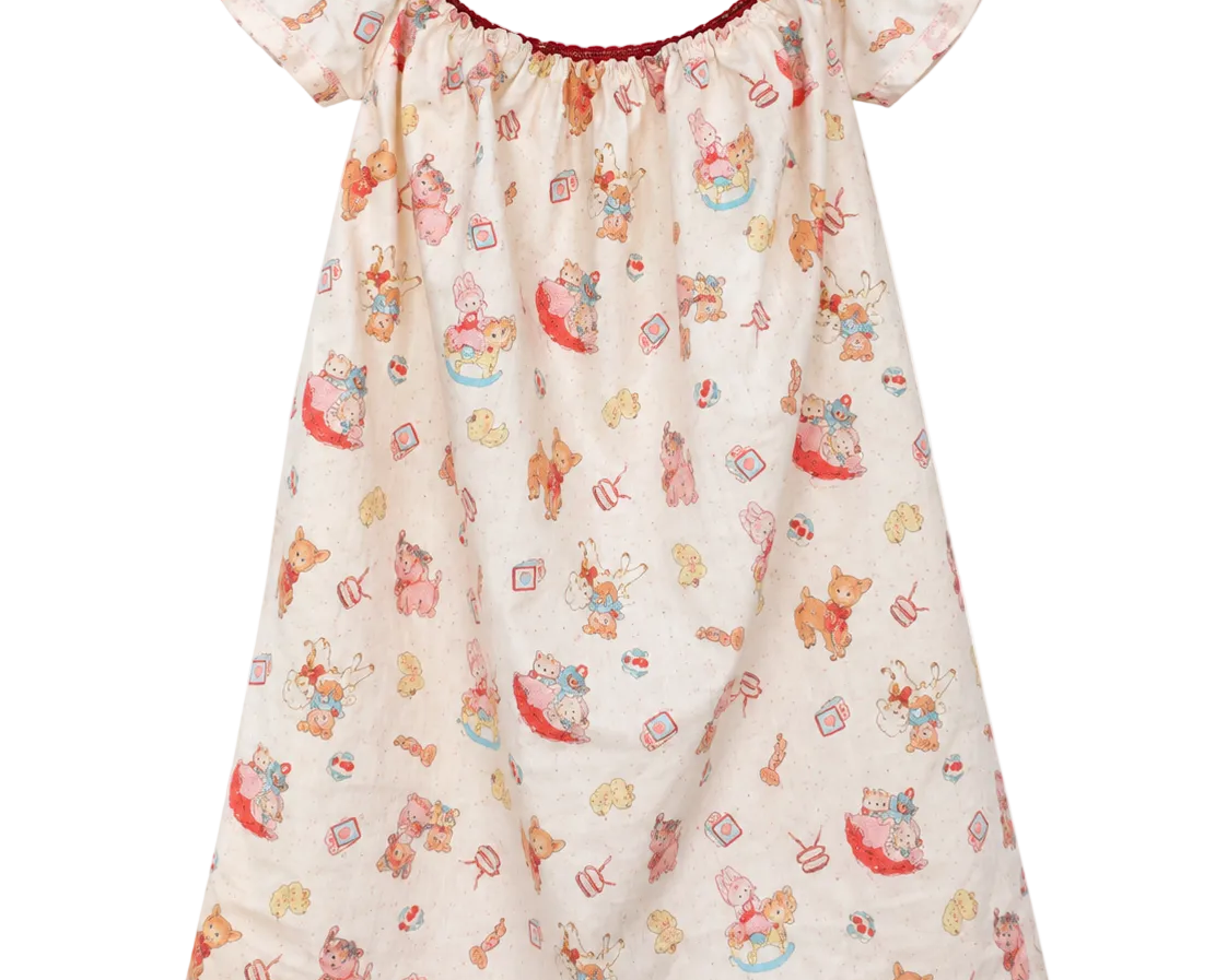 A baby girl's short-sleeve nightgown with a cream-colored base, featuring a playful print of teddy bears, cupcakes, and sweets in red, orange, and blue. It has a ruffled neckline with a thin red trim and a matching ruffled hem.